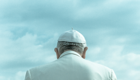 The back view of the Pope in a white cap against a blue cloudy sky